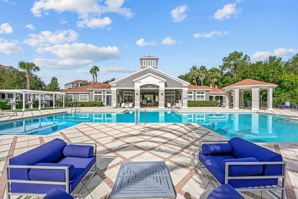 Swimminng pool area featuring stylish outdoor seating, large swimming pool, and elegant clubhouse under a bright blue sky.