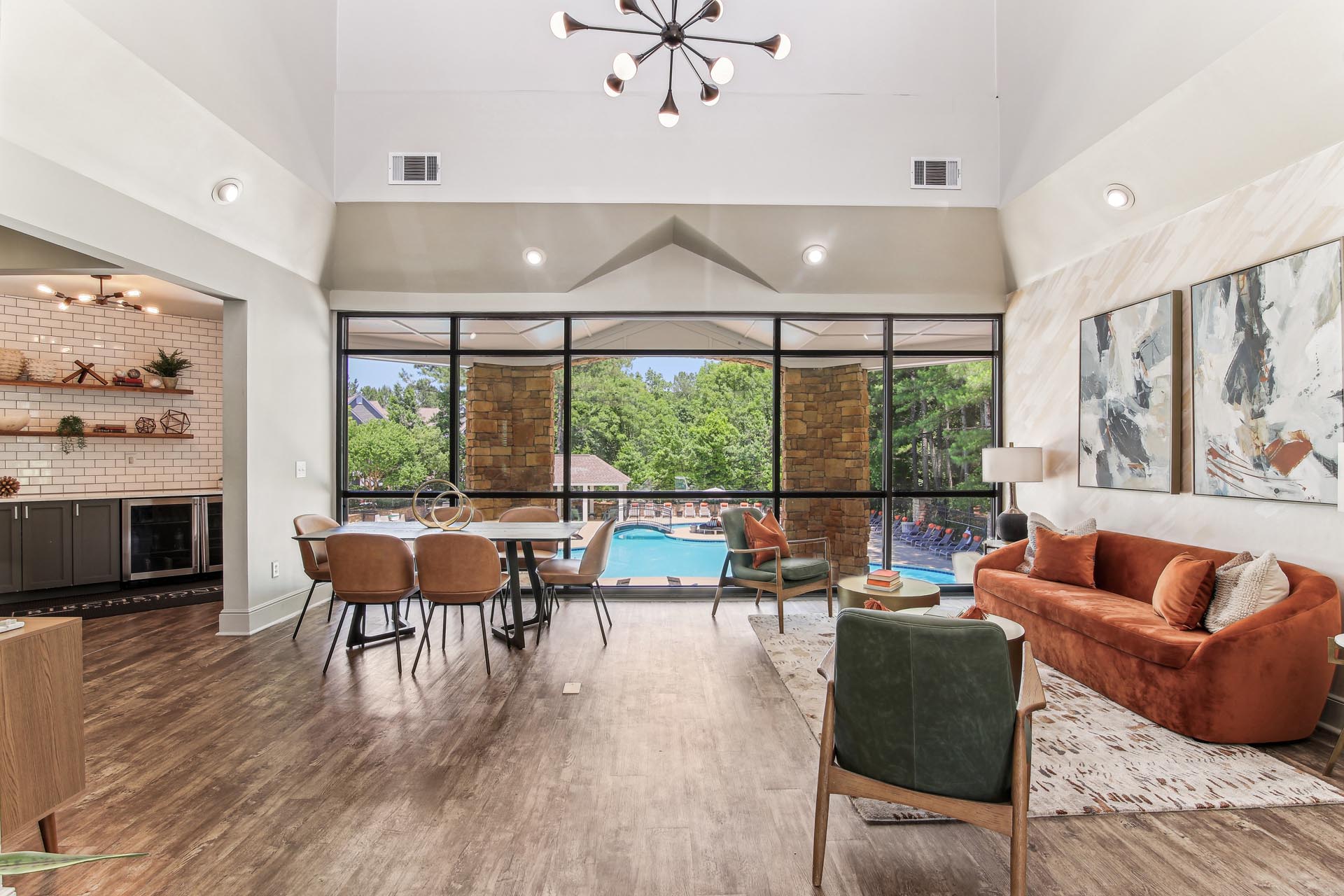 Halston Paces Crossing Clubroom with large table and seating area overlooking the swimming pool with clubroom kitchen in background.