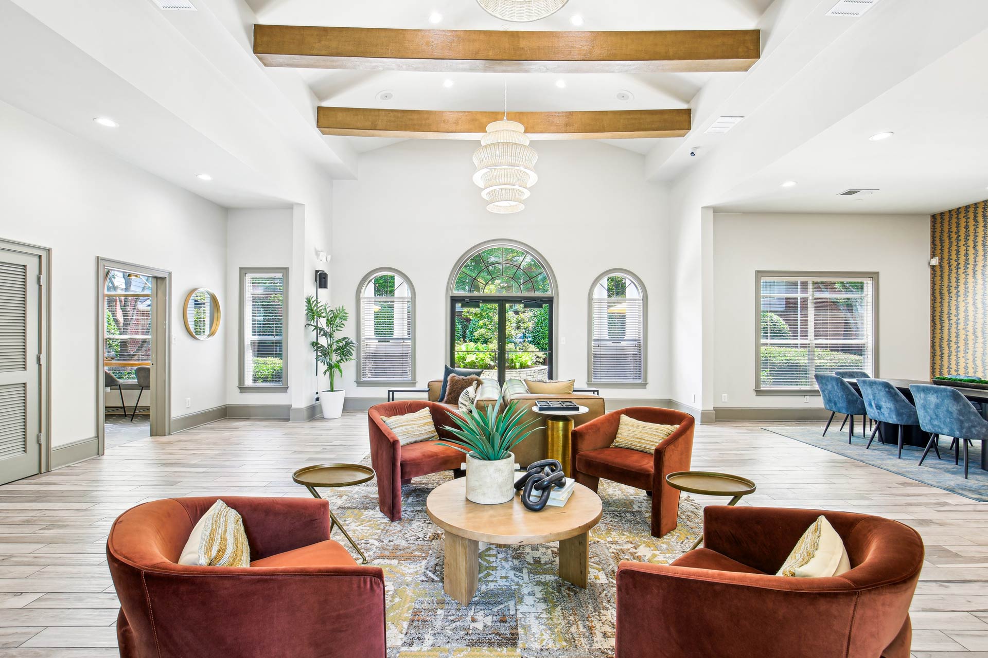 Halston McDonough's clubhouse seating area with four red suede chairs, coffee table hardwood style flooring, high ceiling with wood beams and a chandelier.