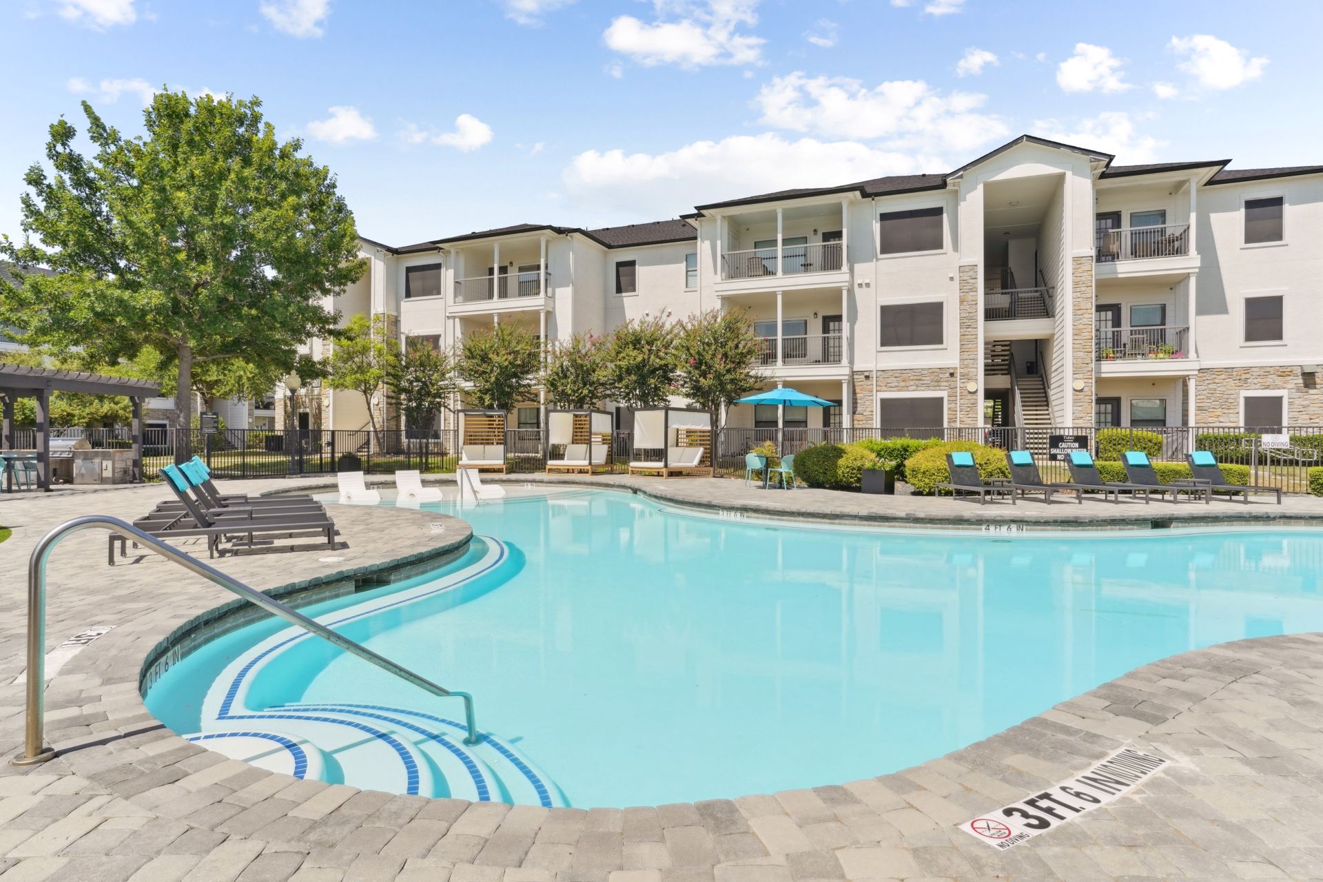 Luxurious apartment complex featuring a sparkling swimming pool, sun loungers, and lush greenery, perfect for a relaxed lifestyle.